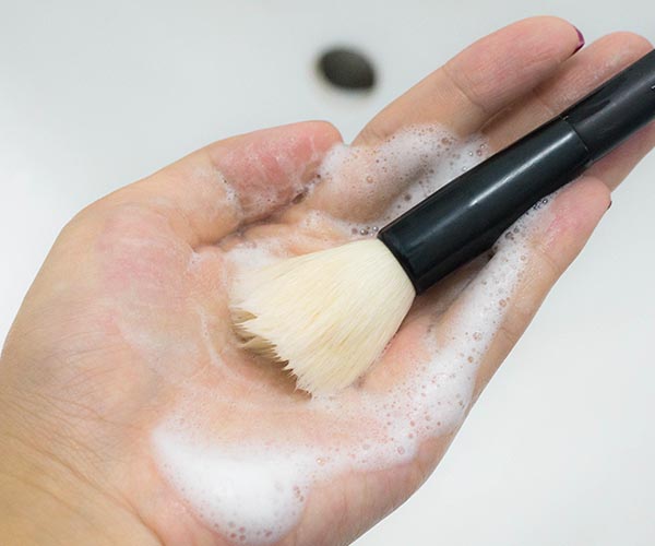 woman washing makeup brush with hand