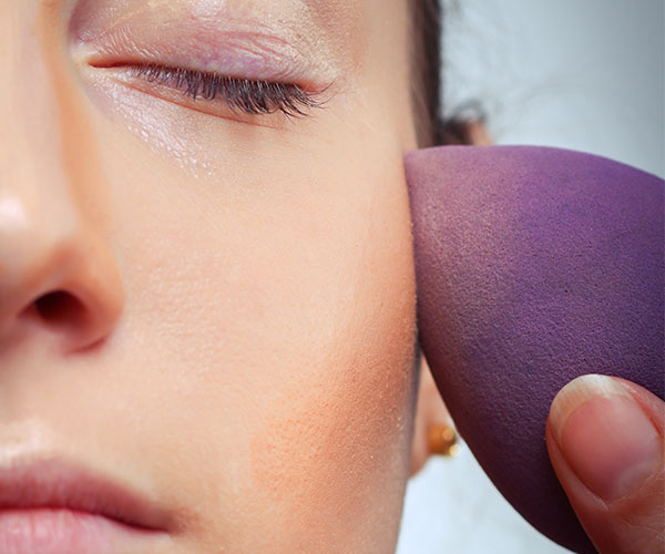 woman applying foundation with purple beautyblender