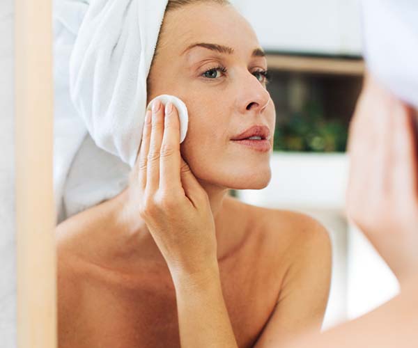 woman applying skincare product in bathroom mirror