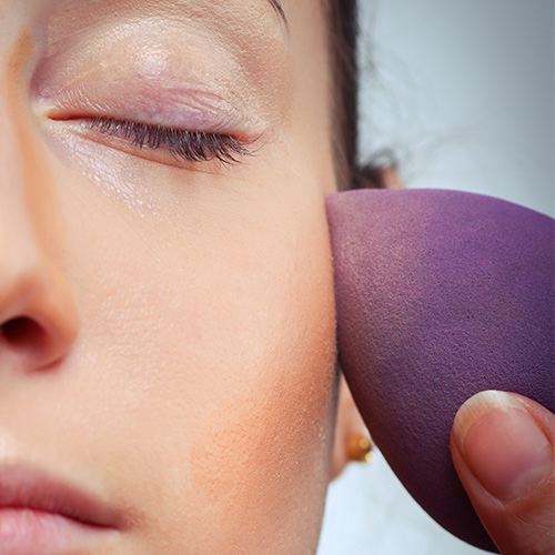 woman applying foundation with purple beautyblender