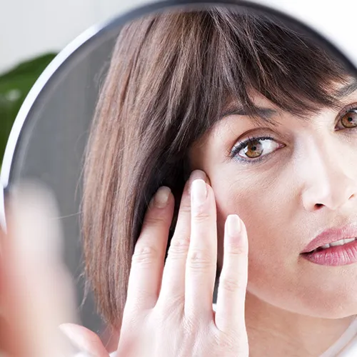 woman applying skincare products in mirror
