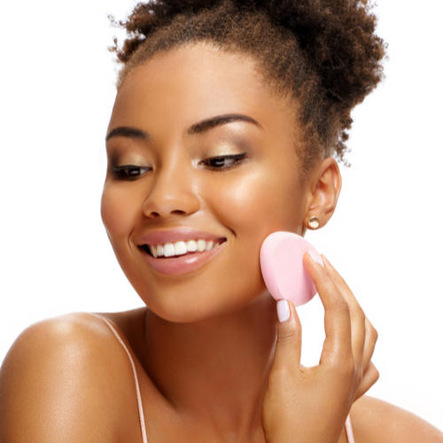 woman applying foundation with a pink makeup sponge