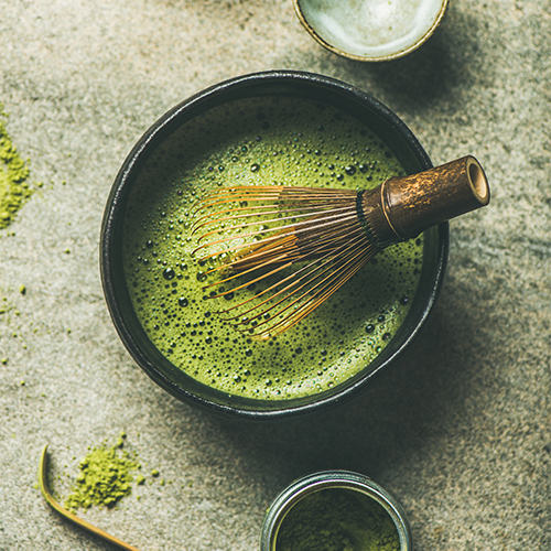 A bamboo whisk in a bowl of matcha.