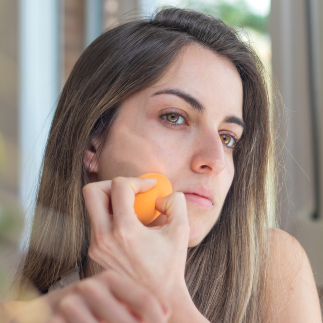 woman applying concealer to skin with beauty blender mirror