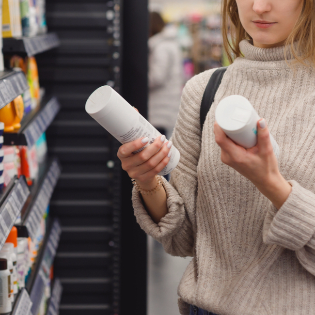 woman shopping comparing hair products store aisle holding bottles