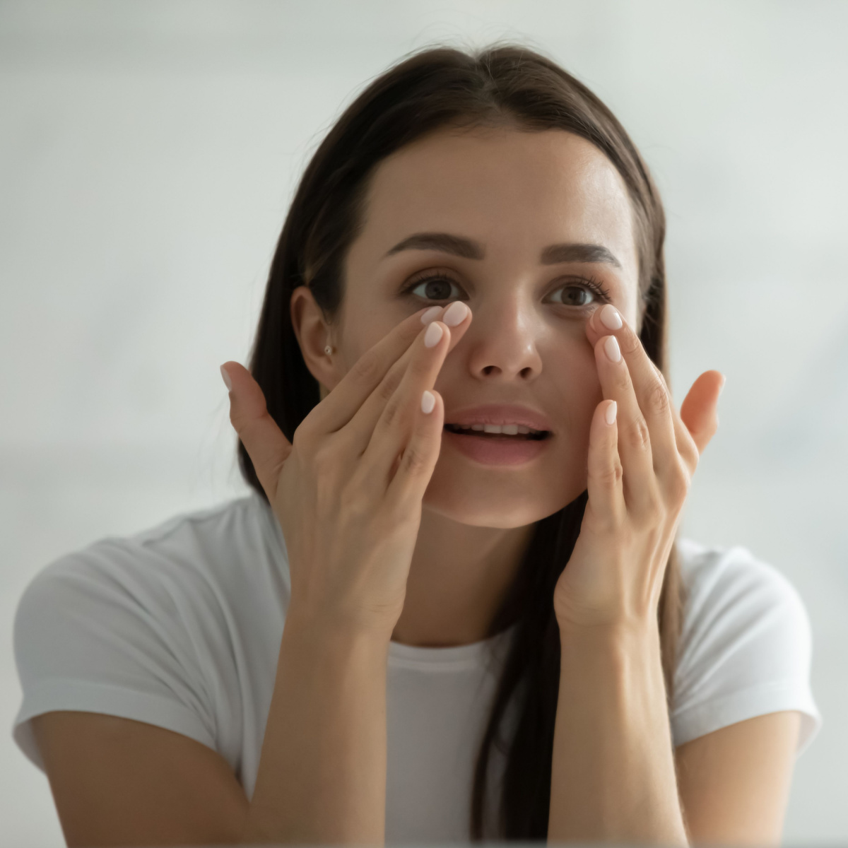 woman touching under-eyes looking in mirror