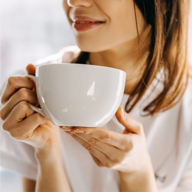 woman drinking tea out of white mug brown hair white sweater hands holding coffee cup