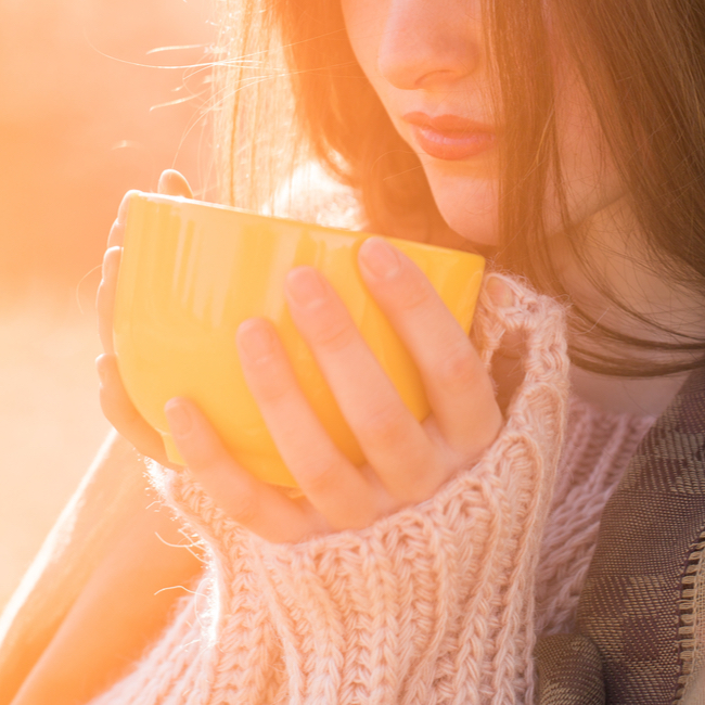 woman drinking mug of tea on cold day white sweater brown hair morning sunlight