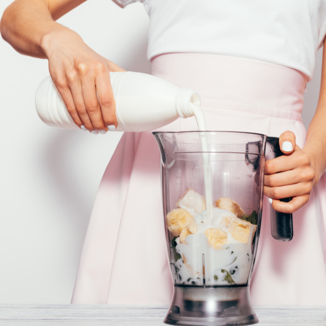 pouring milk from bottle into glass blender smoothie white shirt pink skirt white table