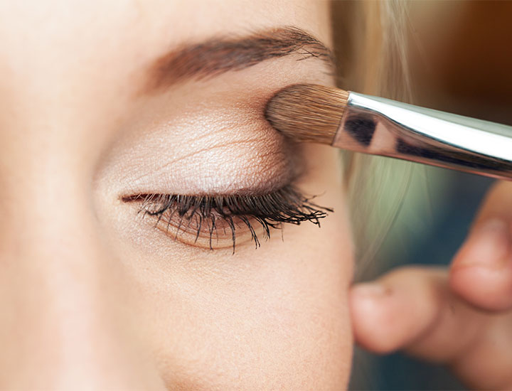 Woman putting on shimmery glittery smokey eyeshadow with brush