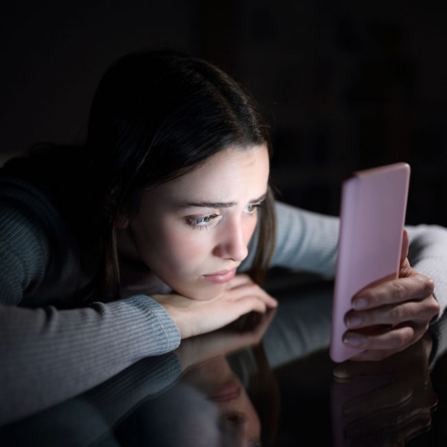 woman at desk in dark looking at phone with a sad expression