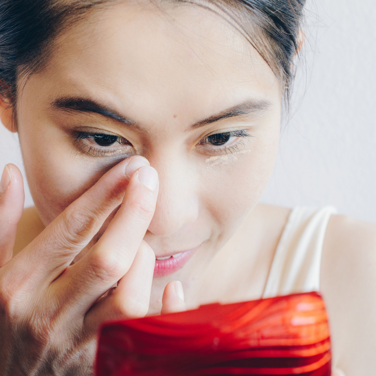 woman applying concealer under eyes with beauty blender looking in compact mirror