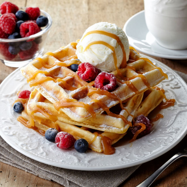 plate of waffles with berries, butter, and syrup