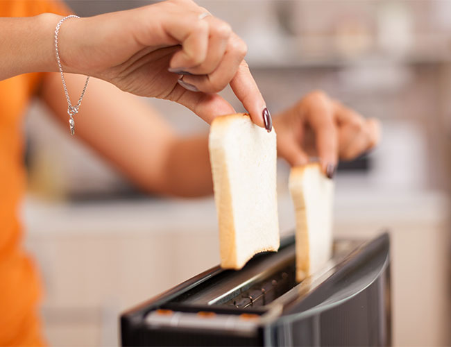 woman putting two slices of white bread into a toaster