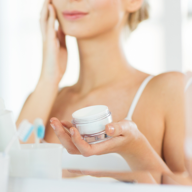 woman applying moisturizer mirror white shirt bathroom