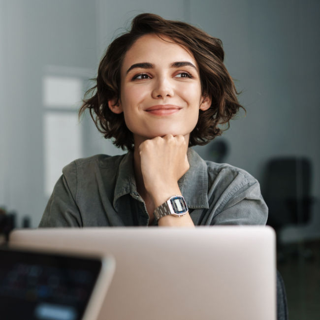 woman looking optimistic and smiling while sitting in front of laptop