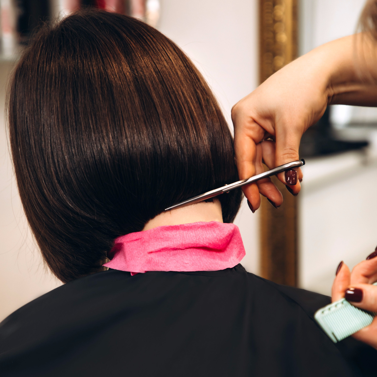 brown-haired woman getting ends of bob trimmed at salon by hairdresser