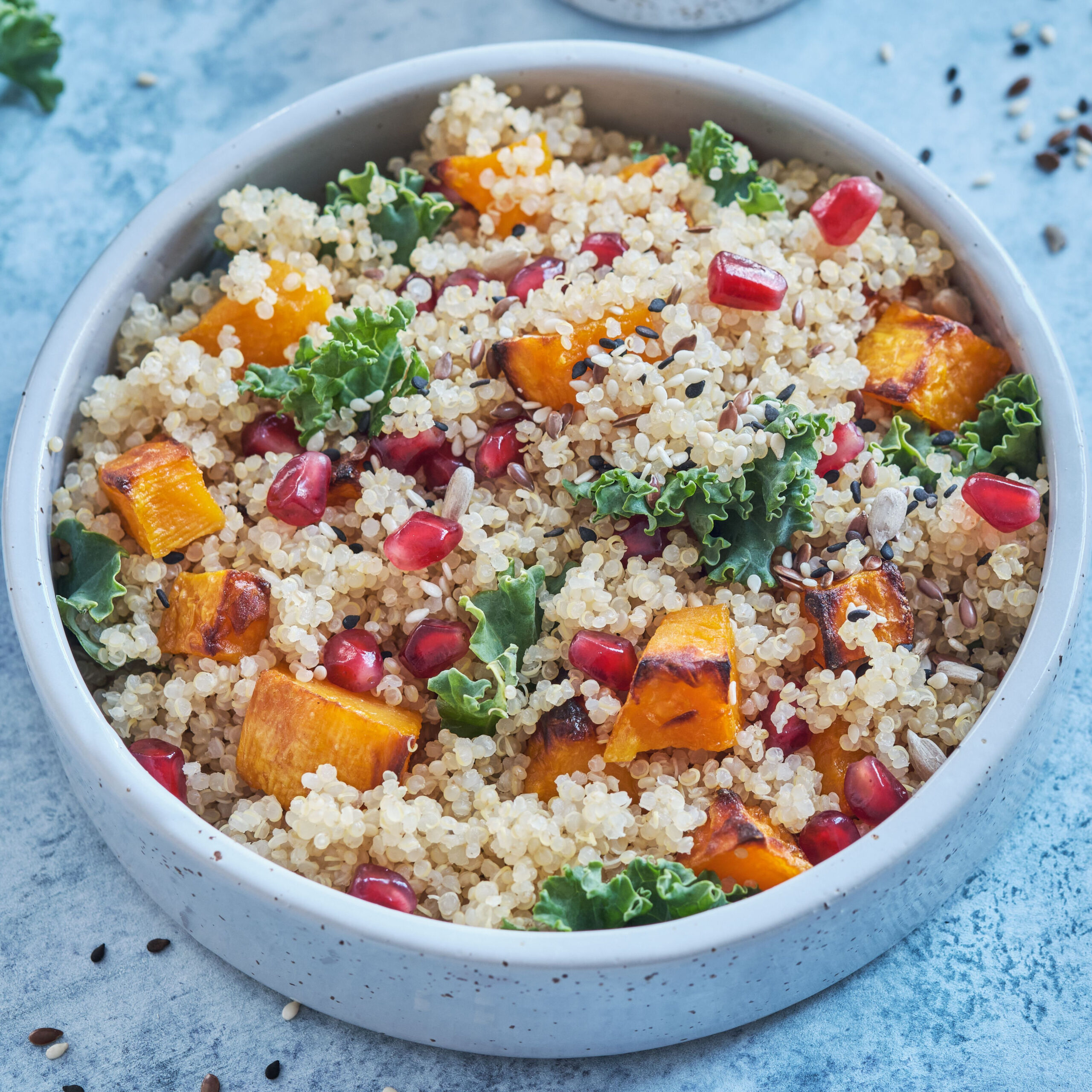 bowl of quinoa with pomegranate, sweet potato, and greens mixed in