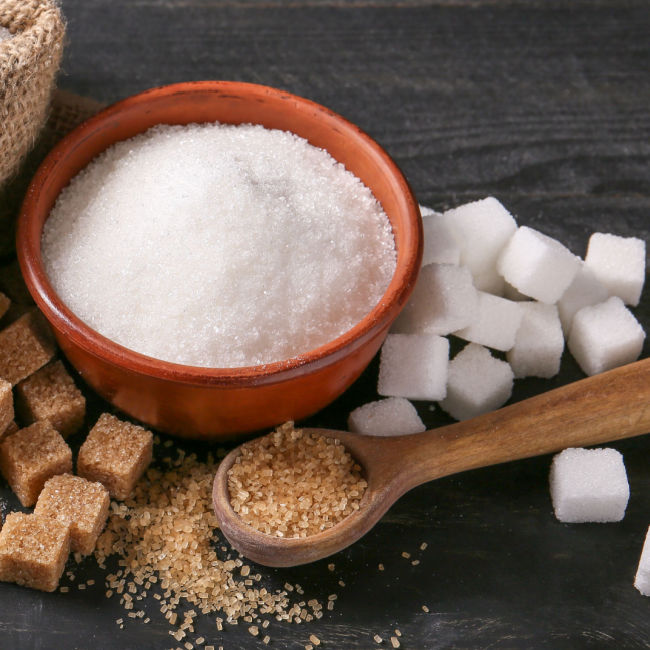 white sugar in bowl next to white and brown sugar cubes and a spoonful of brown sugar