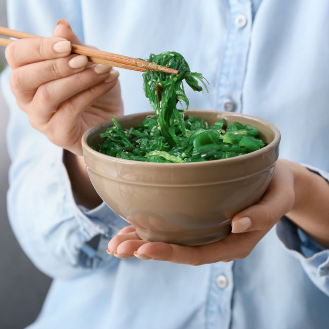 woman eating seaweed salad from bowl with chopsticks