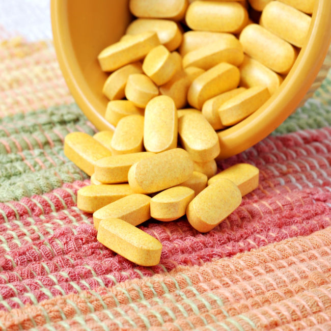 yellow pills spilling out of container on multi-colored cloth