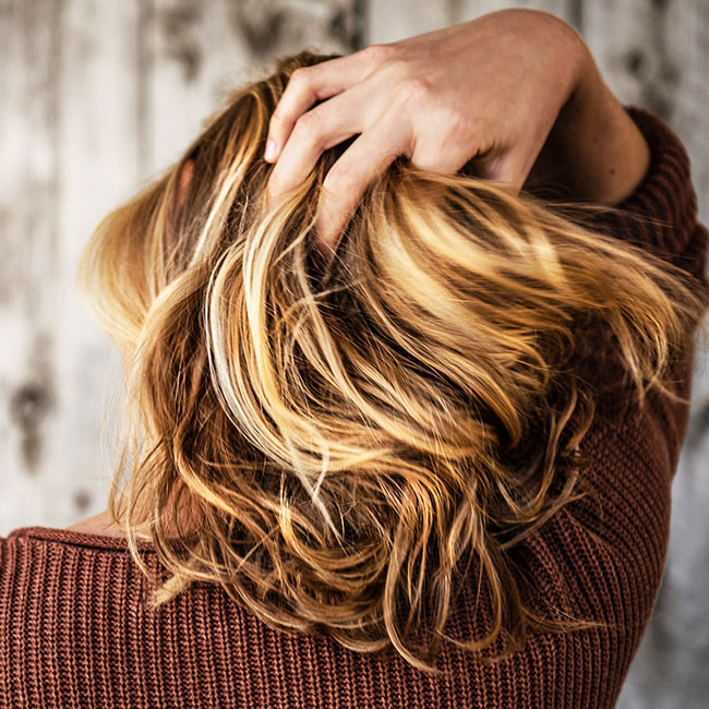 woman running fingers through highlighted blonde hair full voluminous red long-sleeved shirt