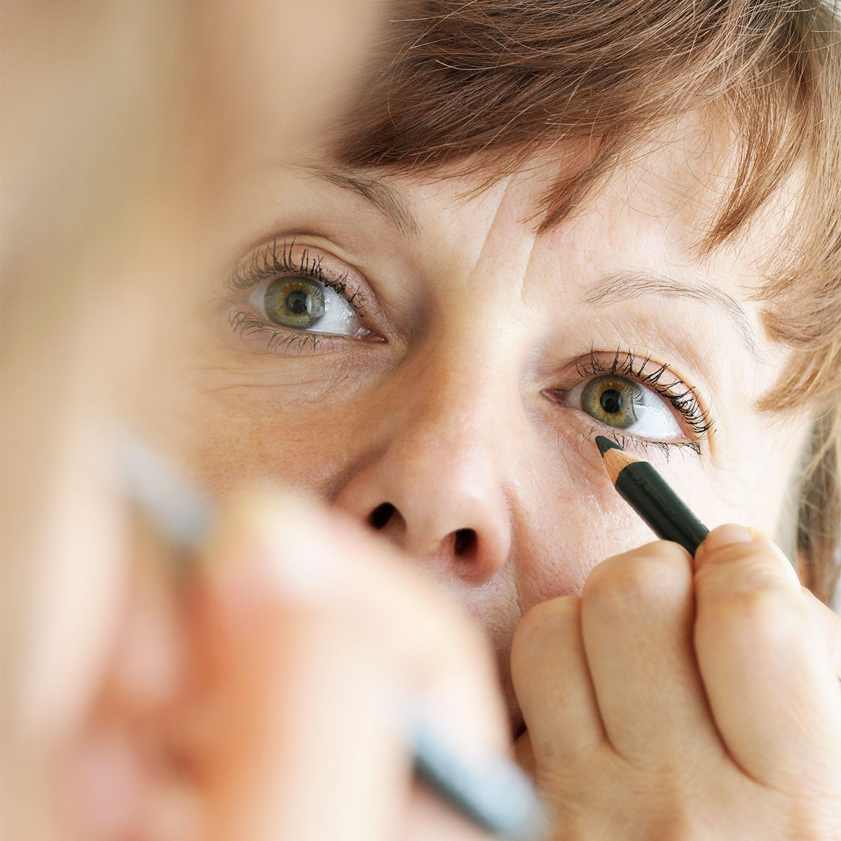 middle aged woman applying black eyeliner to her bottom lash line with black pencil