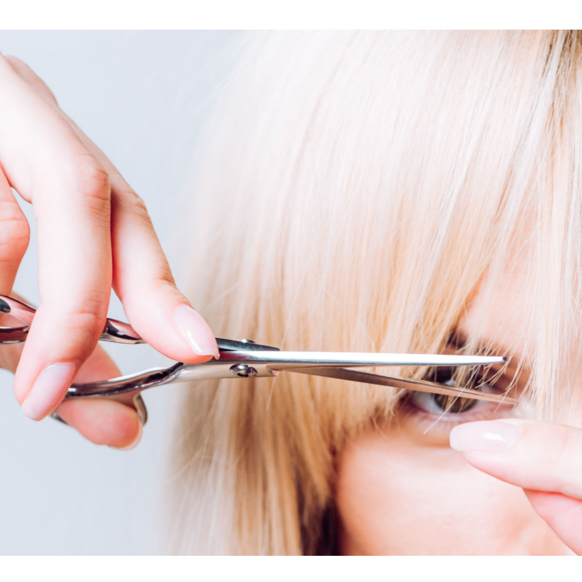 blonde woman trimming her long bangs fringe with silver metal scissors