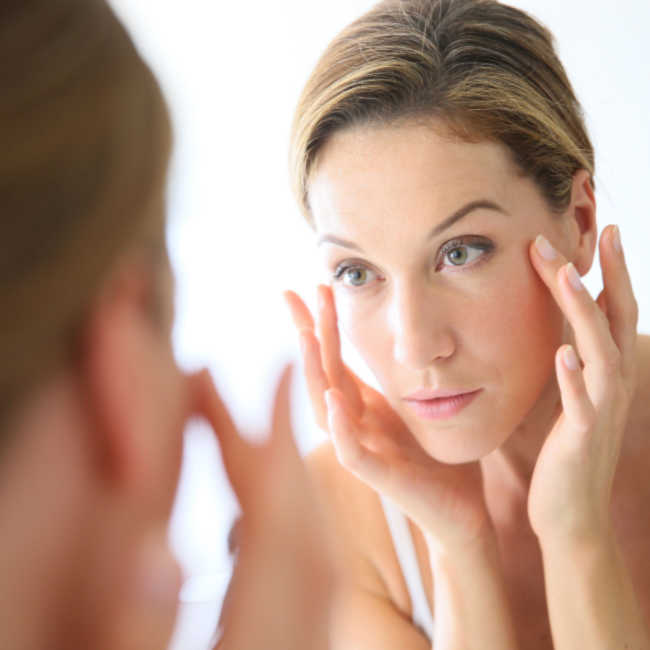 woman examining skin in mirror