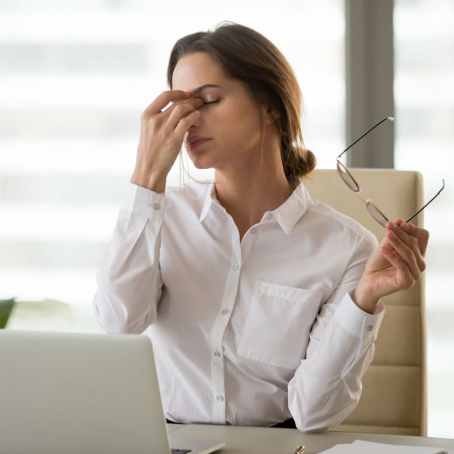 woman sitting at laptop rubbing eyes and holding eyeglasses