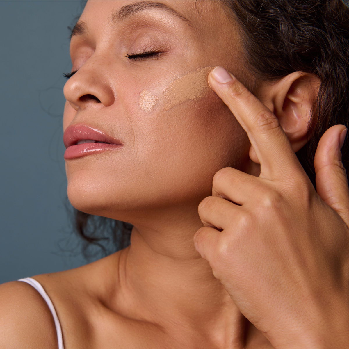 woman applying primer tinted moisturizer to cheek with finger