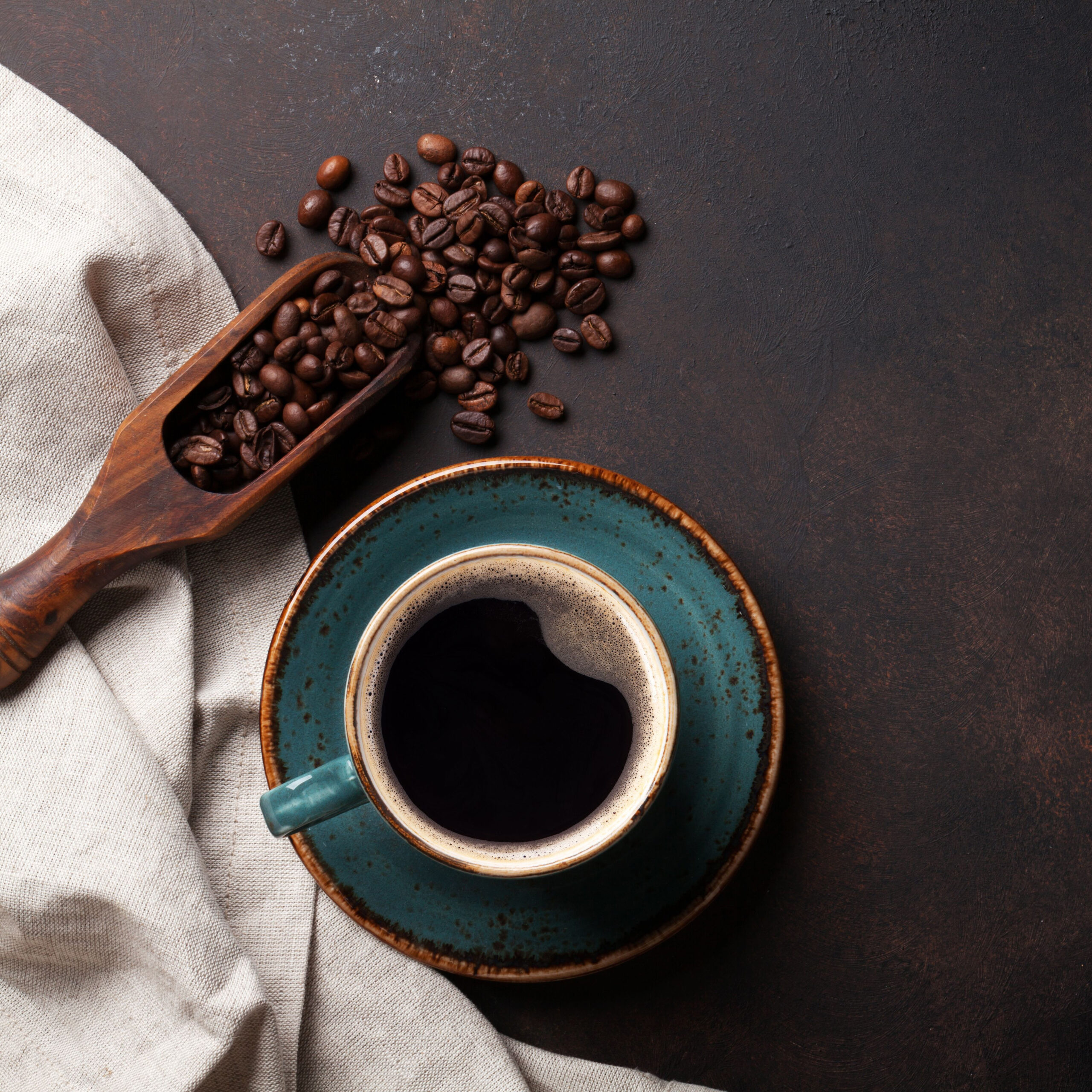 cup of black coffee besides scoop of coffee beans