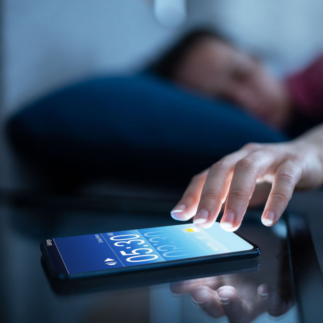 person reaching for phone on nightstand