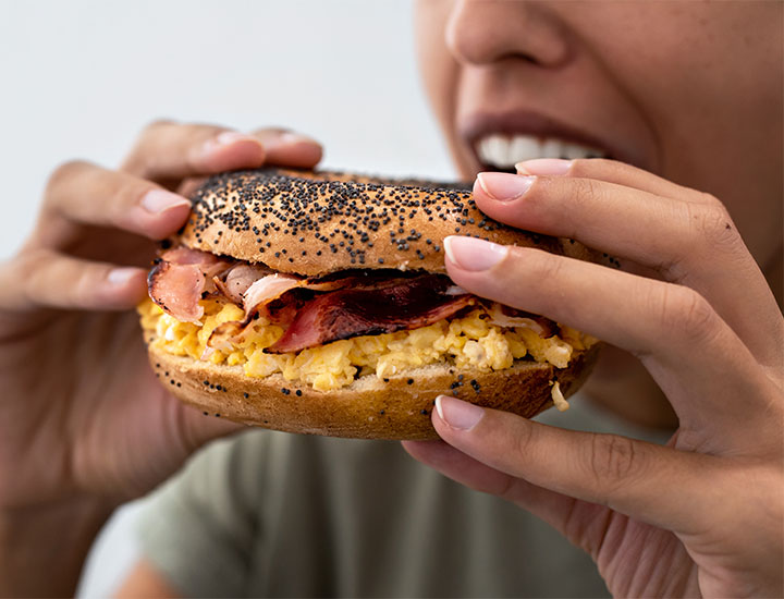 woman biting into bacon egg and cheese bagel