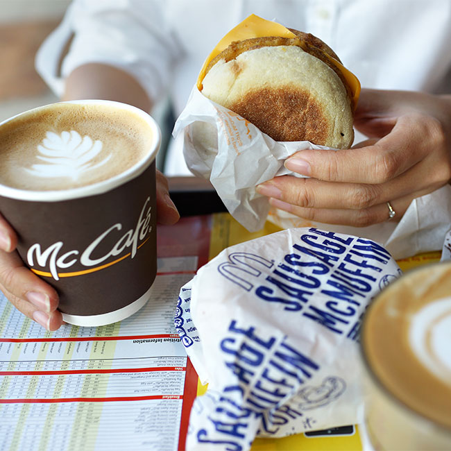 person holding mcmuffin and mccafe coffee