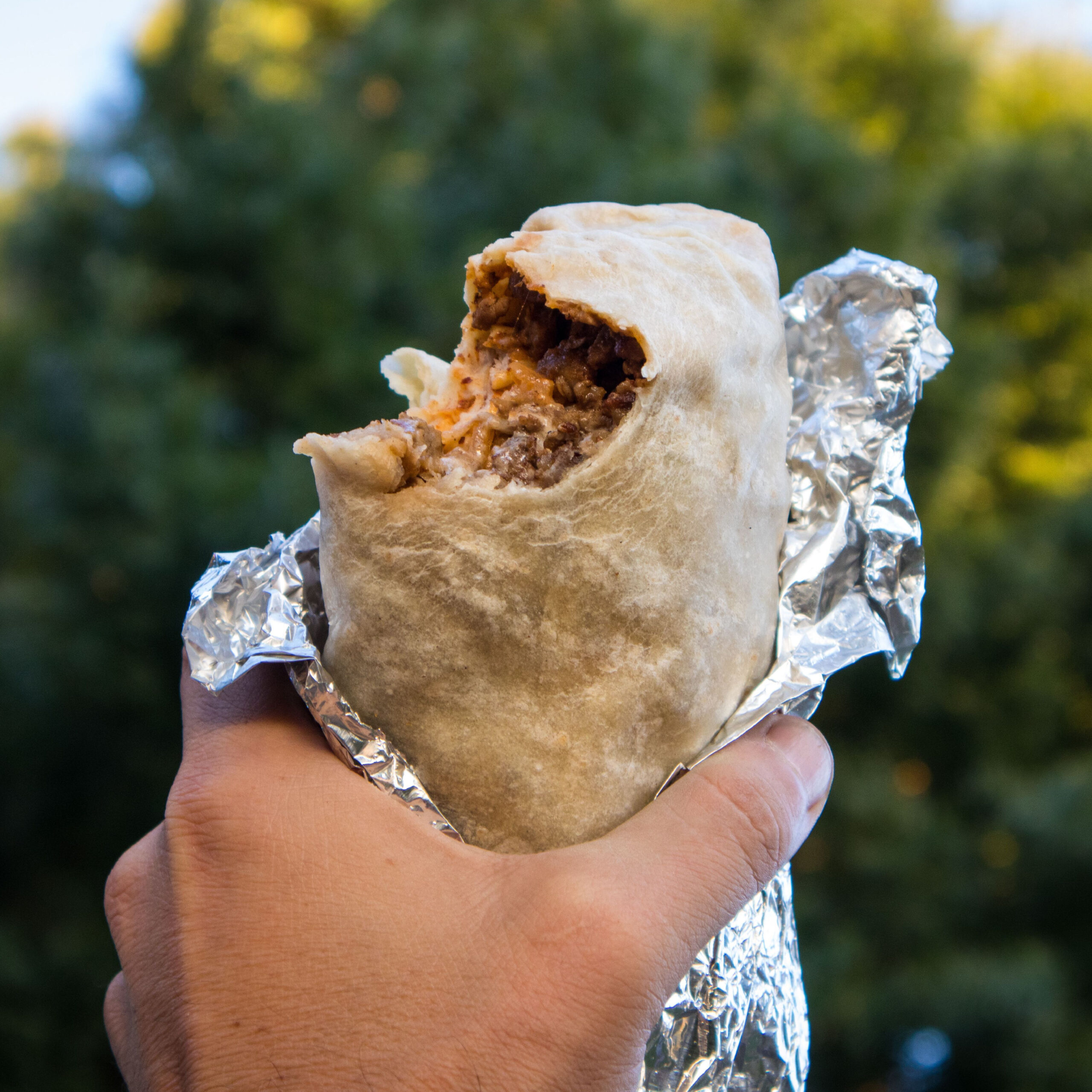 hand holding beef burrito with a bite taken out of it