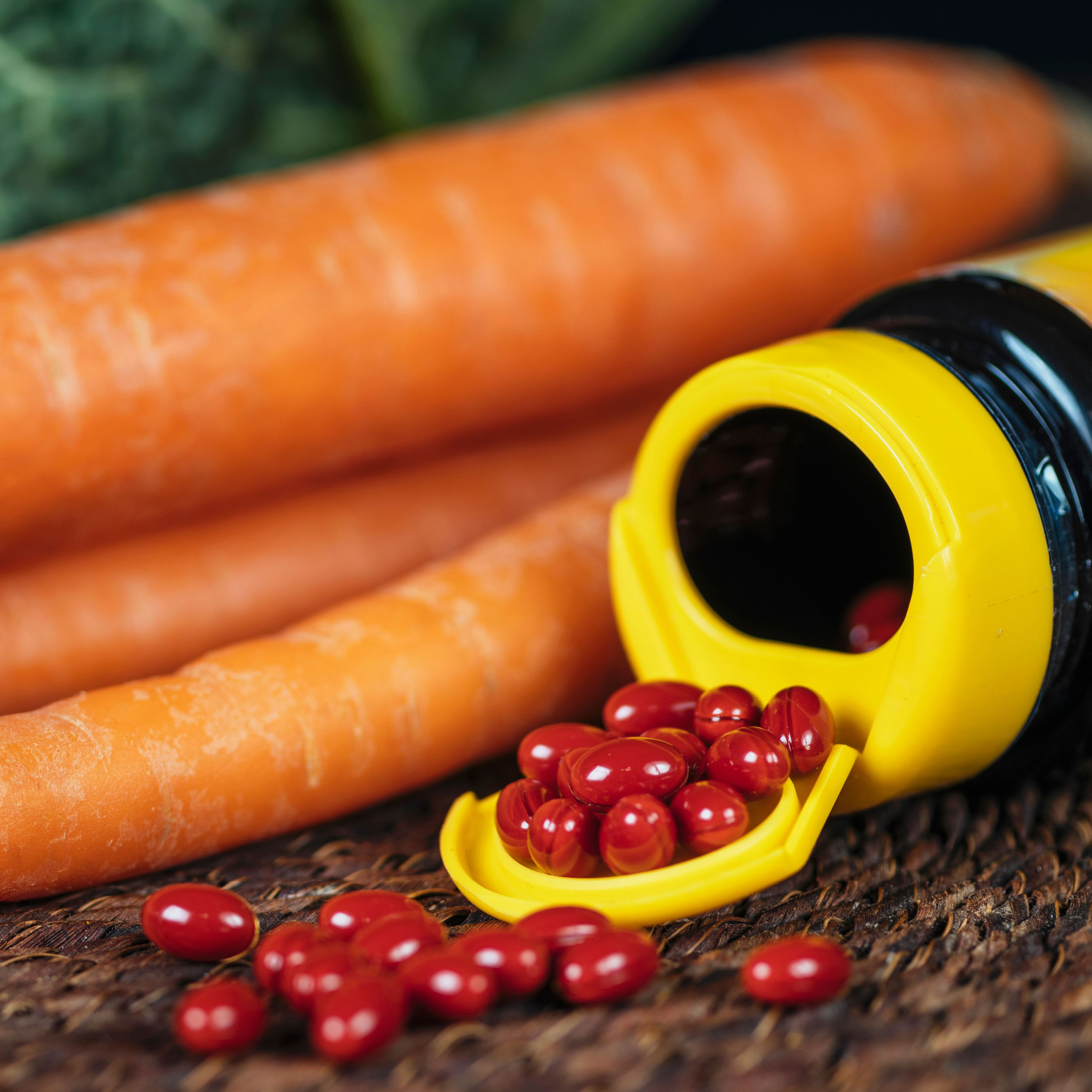 beta carotene supplements spilling out of bottle besides bunch of carrots