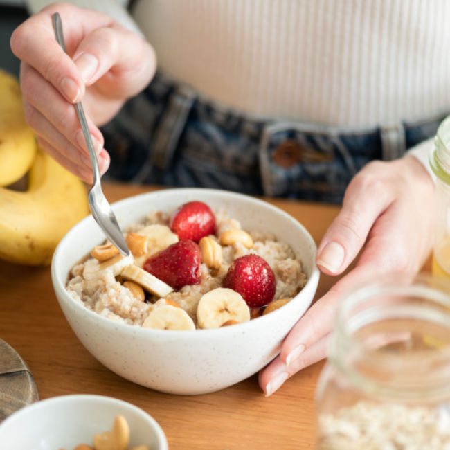woman eating bowl of oatmeal topped with fruit
