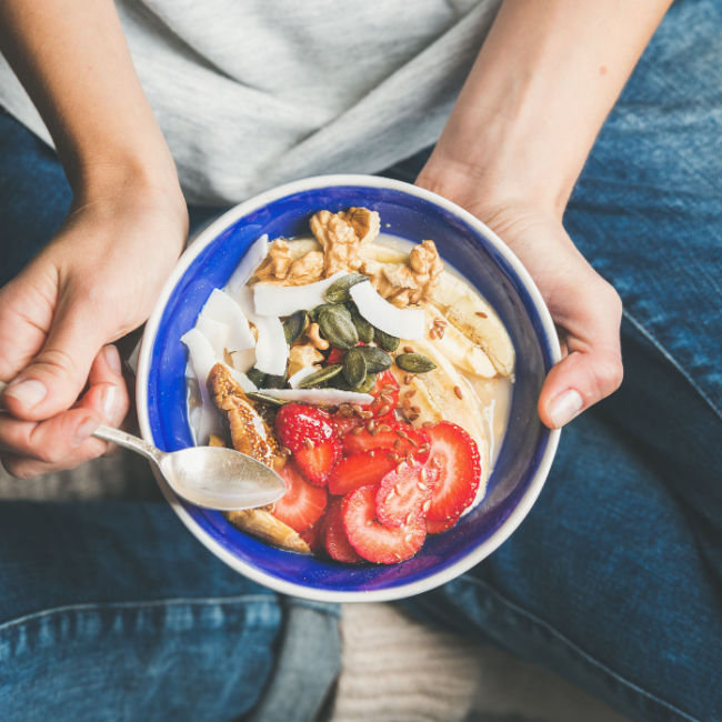 woman eating healthy breakfast of yogurt, fruit, nuts, and more