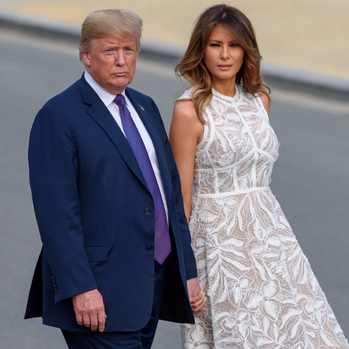 donald trump blue suit blue tie walking with melania trump white flowy dress holding hands