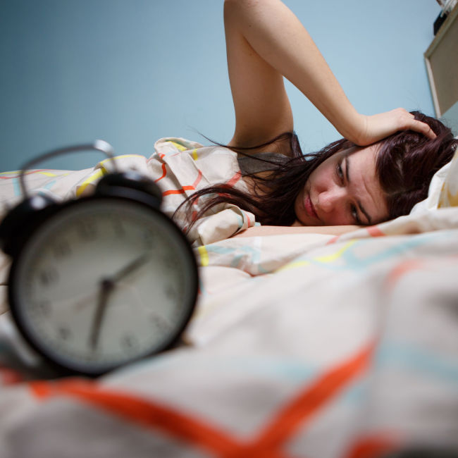 woman waking up in bed beside alarm clock holding head feeling tired