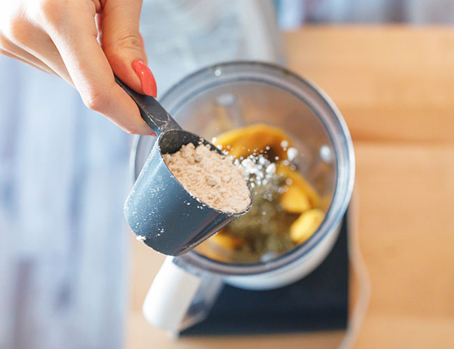 person adding scoop of protein powder to blender