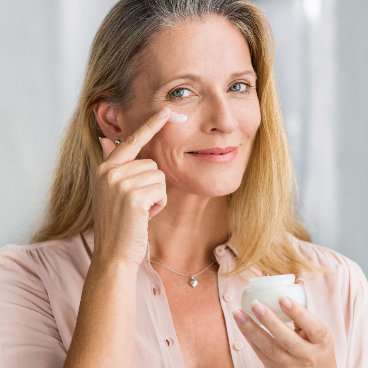 senior woman applying topical cream under eye wrinkled skin finger dipped in cosmetic product