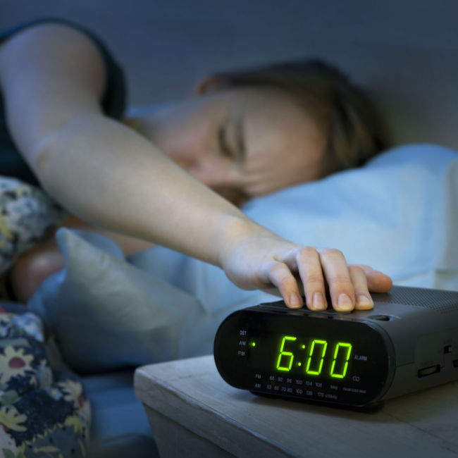 woman hitting snooze on alarm clock in bed