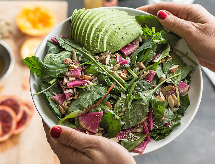 Woman holding a salad with avocado, olive oil, and almonds