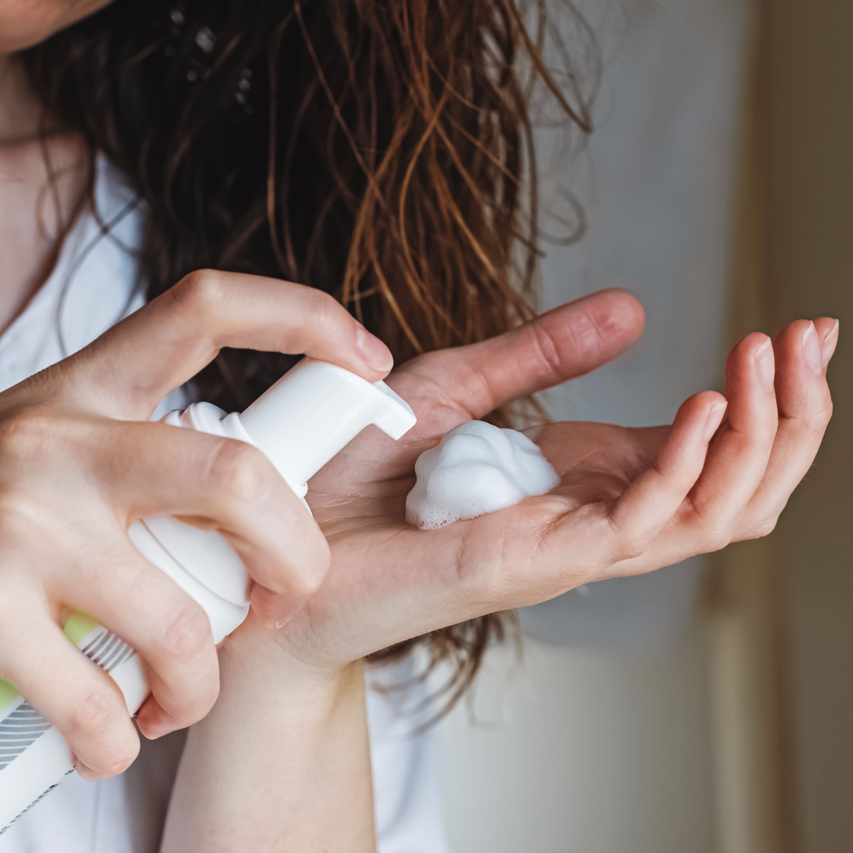 woman applying mousse hair product to wavy brown hair holding product in hand pushing down