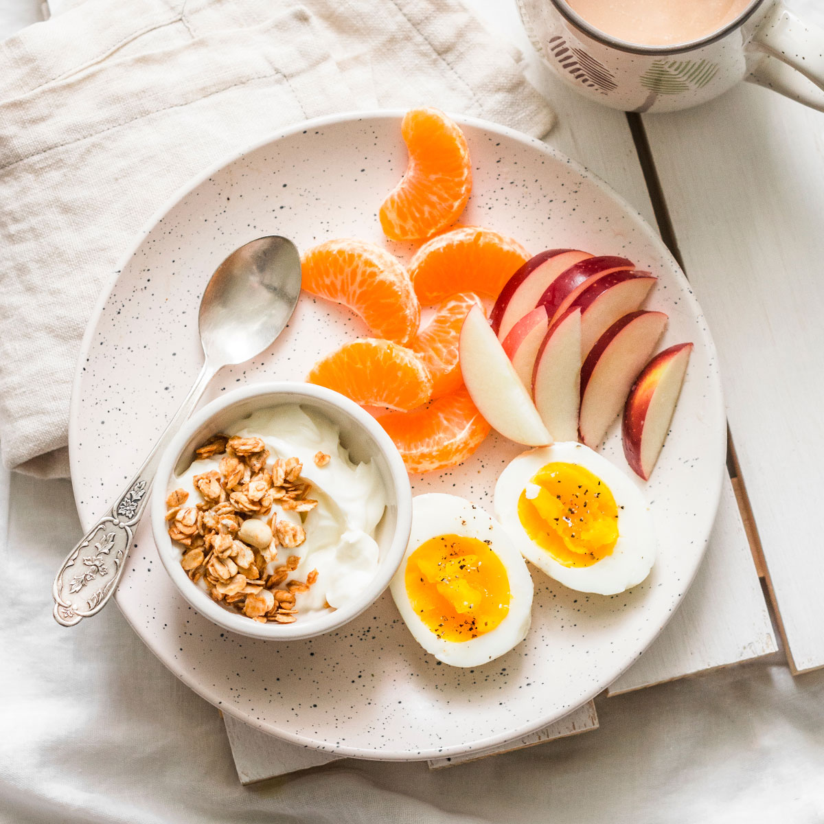 breakfast plate with hard boiled eggs, oranges, yogurt and granola, sliced apples