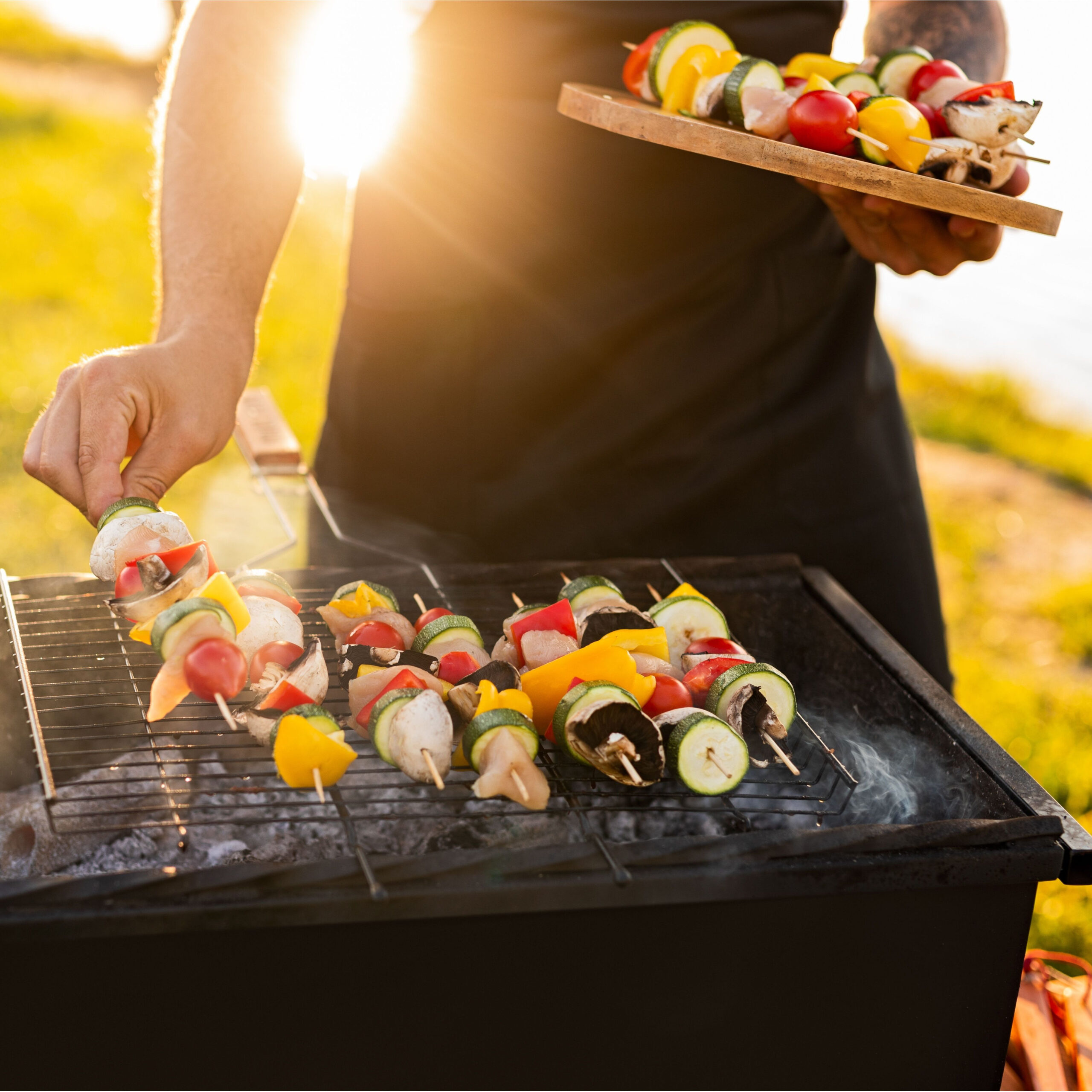 person cooking chicken kebabs on grill