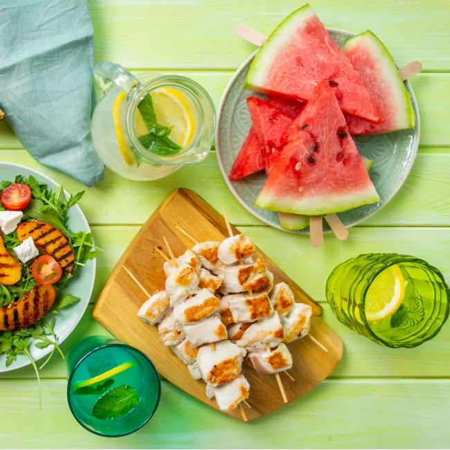 cookout display of chicken kebabs, grilled veggies, and watermelon on green table