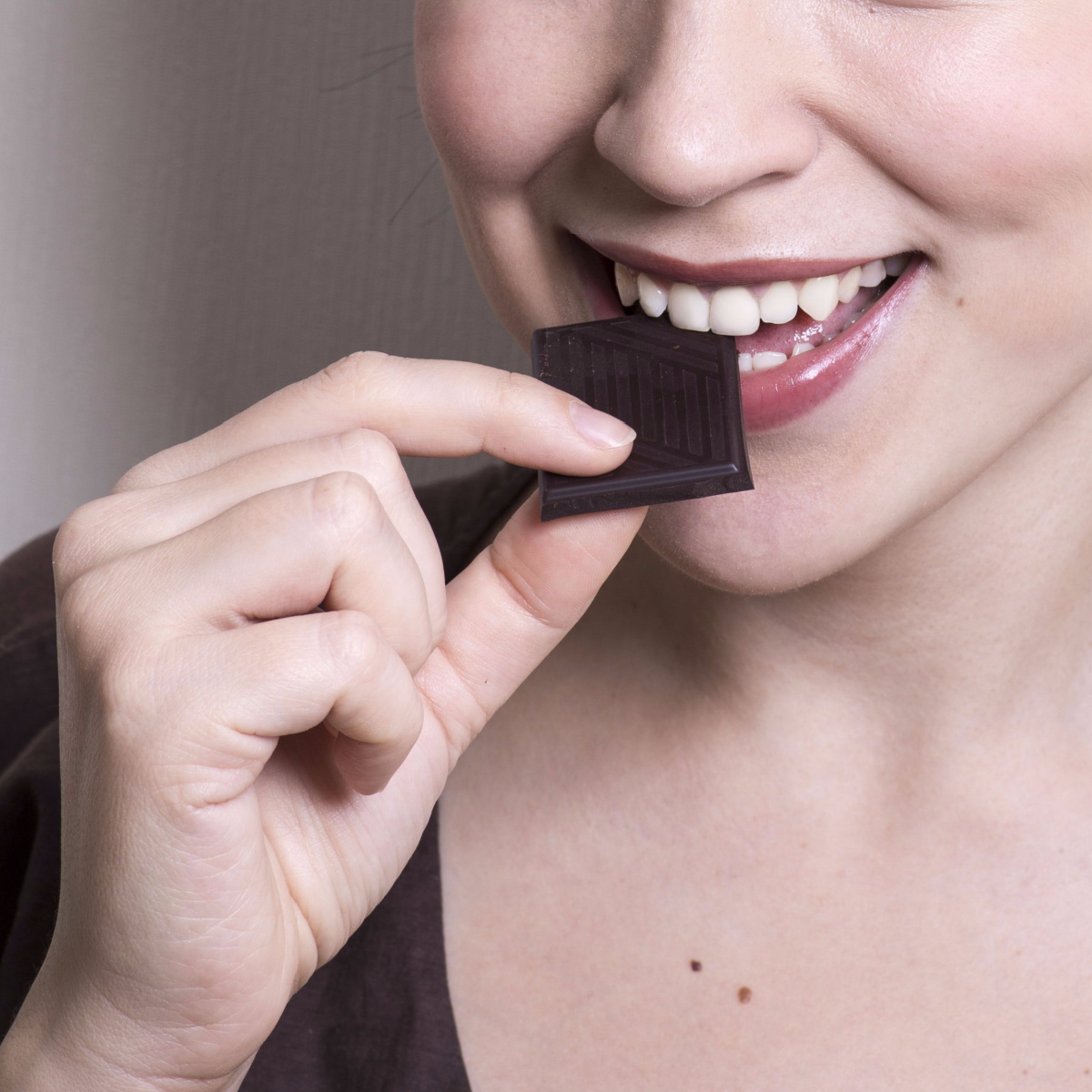 woman biting into dark chocolate square with white teeth red lip gloss